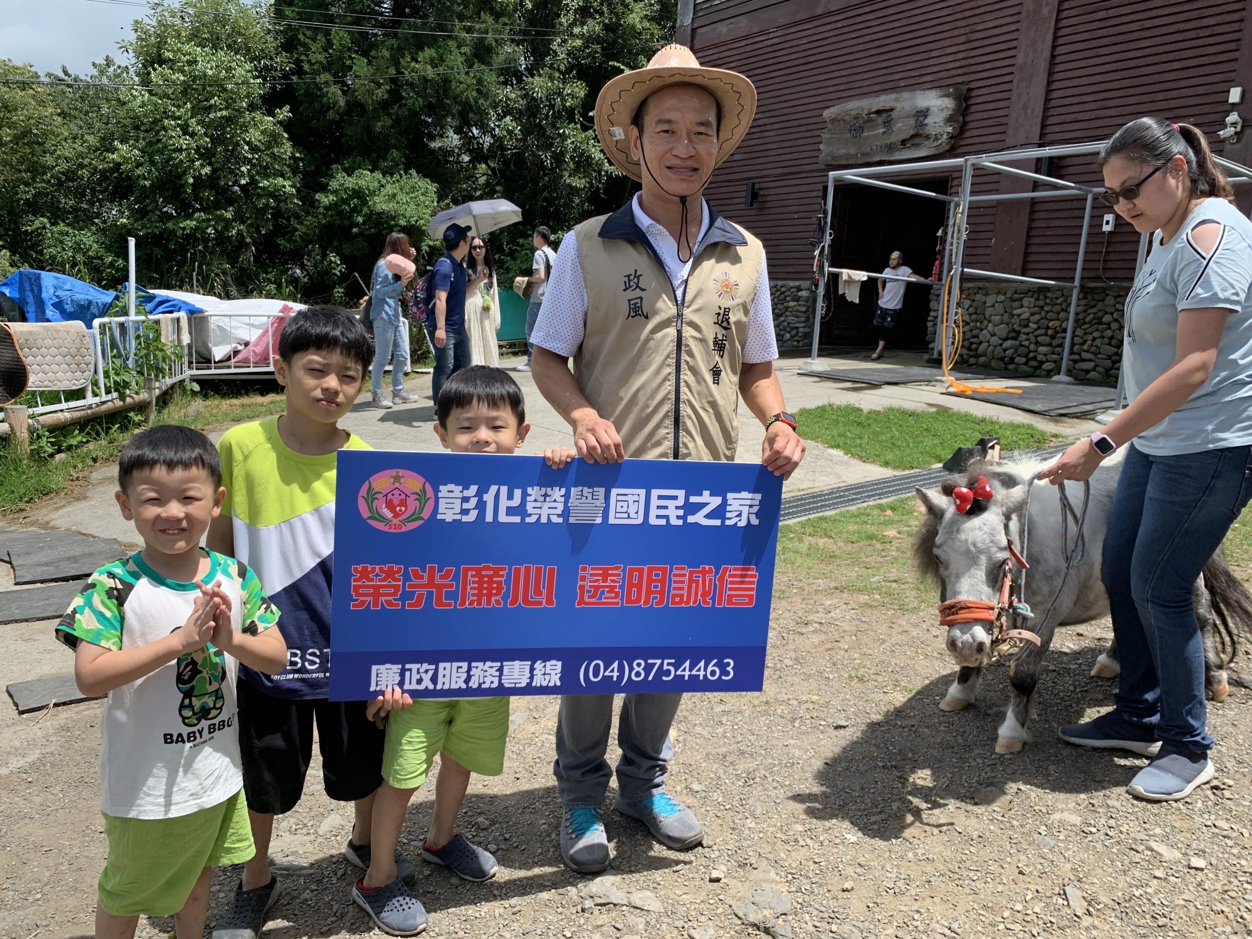 政風室主任劉昌元與學童手持宣導標語與來自荷蘭可供小朋友乘坐的超可愛迷你馬「嚕嚕米」合影。